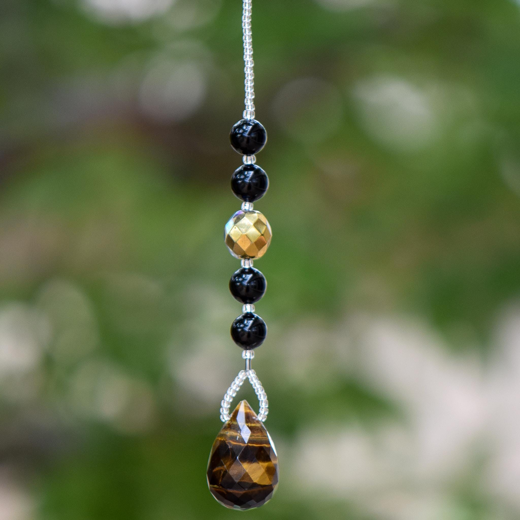 A gold and black beaded car charm with a teardrop-shaped tiger's eye gemstone.