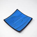 Six inch square glass tray. Center of tray is a medium blue with black streaks. Trim is solid black. On white background.
