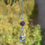 May include: A crystal suncatcher with a silver chain, a clear crystal ball, and a purple and gray stone bead.