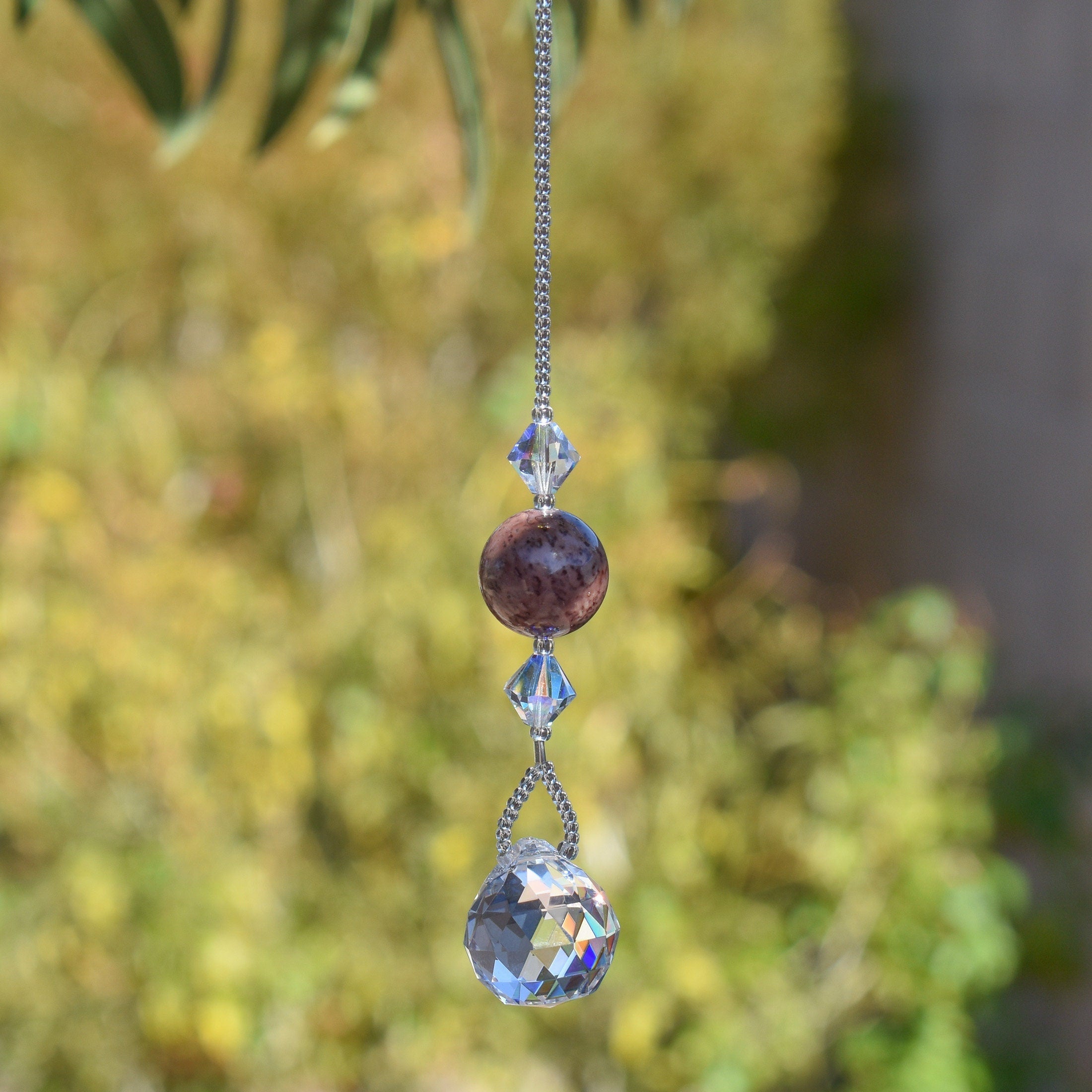 May include: A crystal suncatcher with a silver chain, a clear crystal ball, and a purple and gray stone bead.