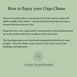 Instructions on how to enjoy a Cinjo Chime. The text is on a light green background. It advises choosing a location with air flow, draping the wire over a nail or branch, and giving the chime room to move. The Cinjo handmade glass art logo is at the bottom.