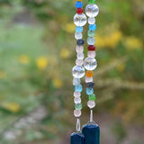 Brightly colored glass beads from Ghana, South Africa&#39;s Krobo tribe are strung with large solid clear glass beads, hanging in front of blurred foliage background. Two pieces of deep aqua blue fused glass are at each end of the long wire.