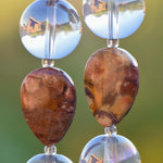 Close up view of two Birds Eye Rhyolite stone beads, each flanked by two larger clear glass reflective beads.