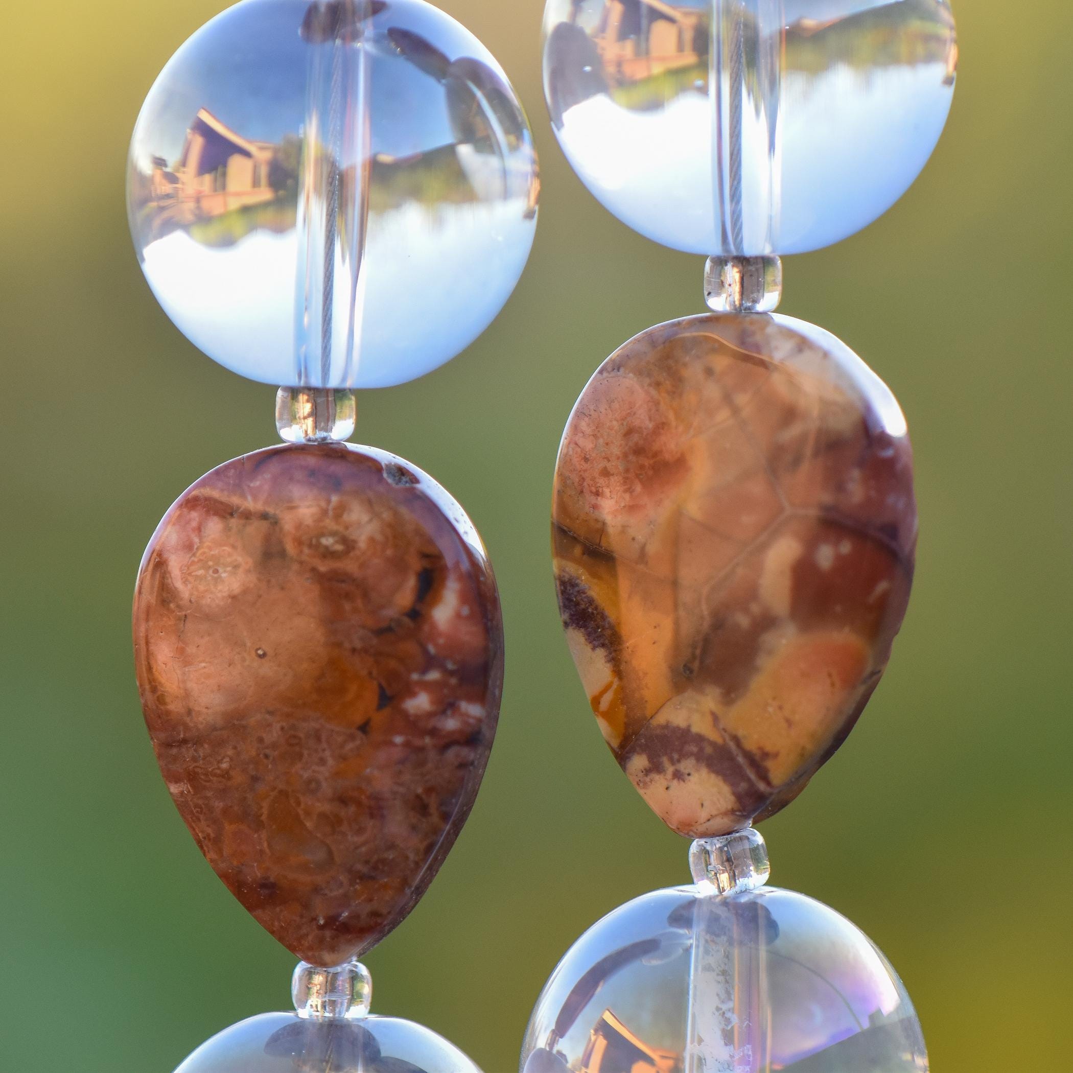 Close up view of two Birds Eye Rhyolite stone beads, each flanked by two larger clear glass reflective beads.