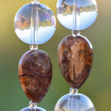 Close up view of two Birds Eye Rhyolite stone beads, each flanked by two larger clear glass reflective beads.