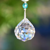 Closeup of large, mostly round faceted glass crystal prism with one turquoise glass bead above, connected by stainless steel wire covered in silver-lined seed beads.