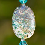 Close up view of large, oval stone azurite malachite stone bead against blurred green background. Stone is mostly white and tan or brown with streaks of green.