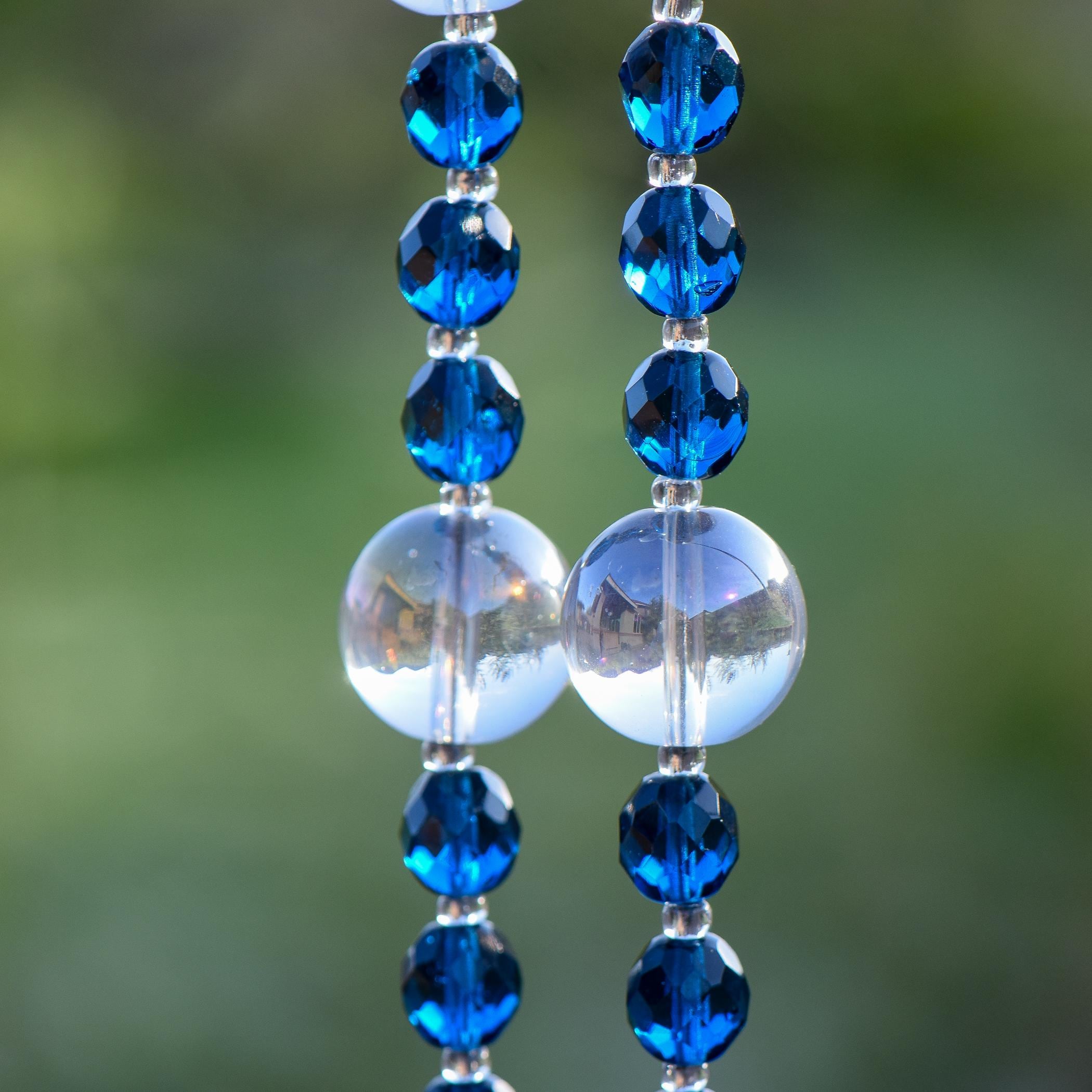Two large clear lamp worked glass beads flanked by smaller, faceted dark aqua glass beads.