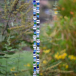 A beaded wind chime with a variety of colorful beads. The beads are primarily clear, blue, and green, arranged in a vertical pattern. The beads are round and transparent, creating a decorative and eye-catching design. The wind chime is used for outdoor decoration.