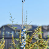 A decorative wind chime with a wire covered in silver-lined seed beads with blue and clear beads. The wind chime features a series of blue glass beads and oval-shaped stones in shades of blue and gray. The beads and stones are strung together, creating a visually appealing and elegant design.