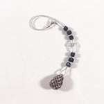 Small purple murano glass sun catcher laying flat on white background. Sun catcher has six purple murano cube beads flanking a glass crystal cross and anchored by a large sterling silver pendant. At the top of the sun catcher is a seed bead-covered wire ending in a silver plated clasp