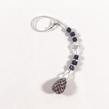 Small purple murano glass sun catcher laying flat on white background. Sun catcher has six purple murano cube beads flanking a glass crystal cross and anchored by a large sterling silver pendant. At the top of the sun catcher is a seed bead-covered wire ending in a silver plated clasp