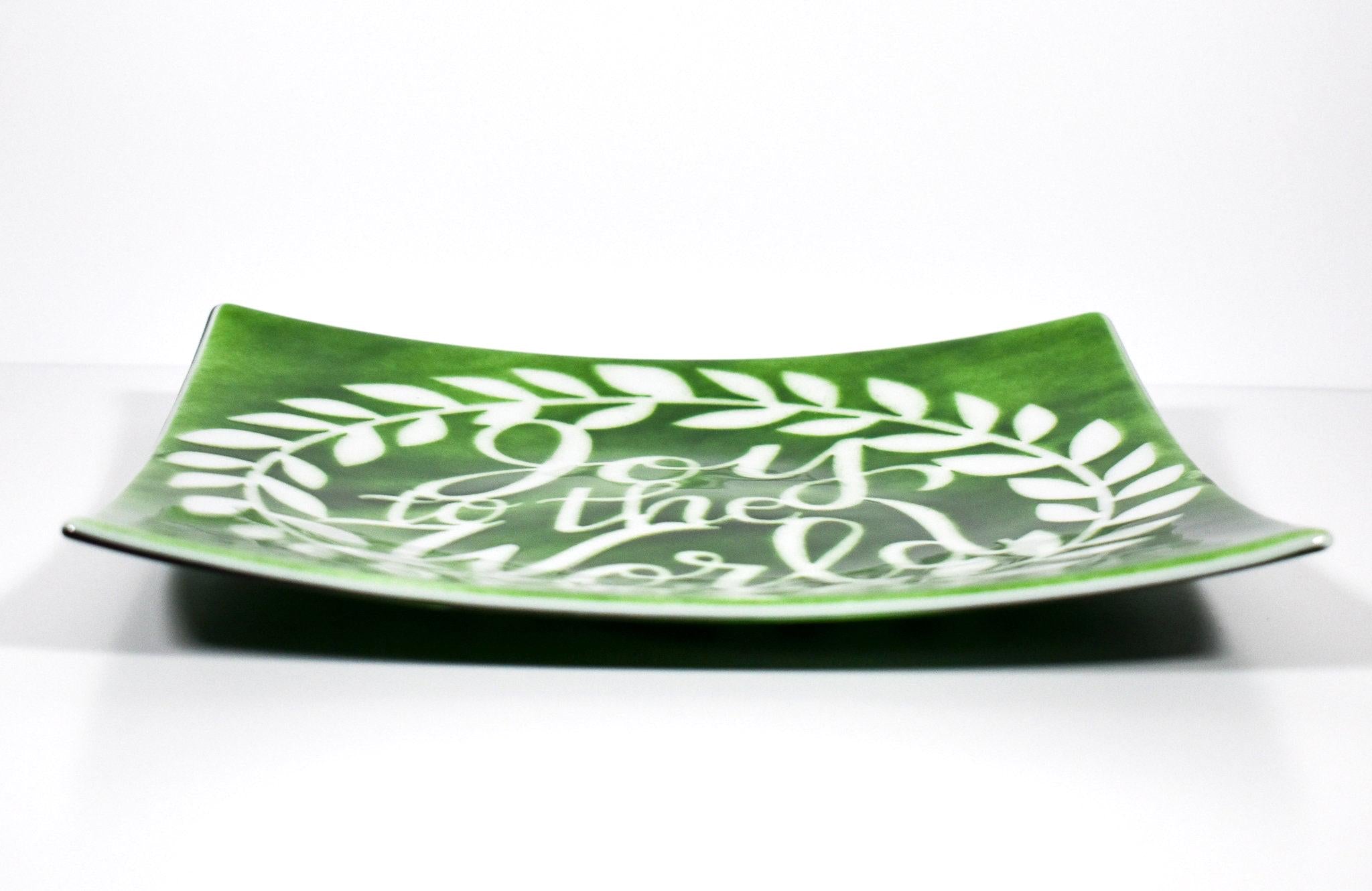 A square green glass serving tray with a white design of a wreath and the words &#39;Joy to the World&#39;. Viewed from the side with tray flat on white background.