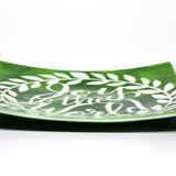 A square green glass serving tray with a white design of a wreath and the words &#39;Joy to the World&#39;. Viewed from the side with tray flat on white background.