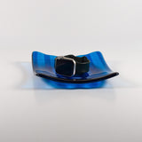 Deep aqua blue fused glass tray with two opposite scalloped edges and strips of a lighter color. The photo is looking at the front of the tray and the tray is on a white surface. The tray is holding a watch to show size and use.