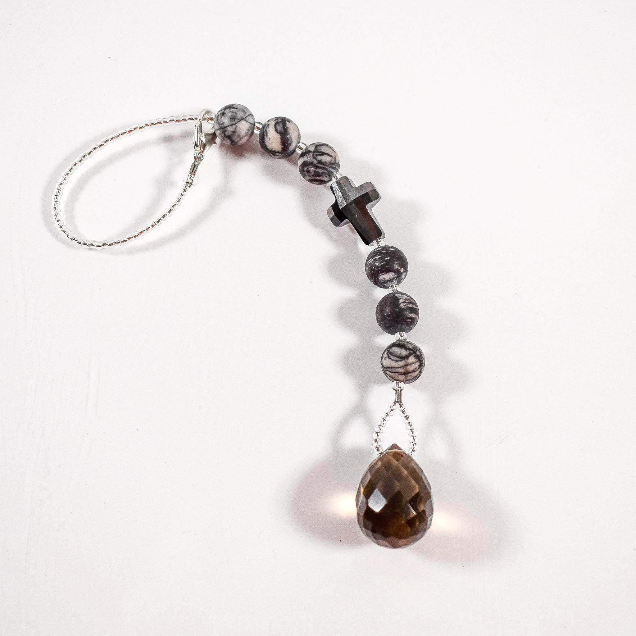 Small sun catcher hanging vertically against white background. Silver-gray crystal cross is flanked by six jasper stone beads in a marbled gray, anchored by large smoky quartz pendant