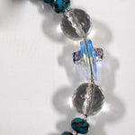 Close up view of crystal cross bead flanked by two round, faceted glass crystal beads, on white surface.