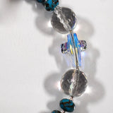 Close up view of crystal cross bead flanked by two round, faceted glass crystal beads, on white surface.