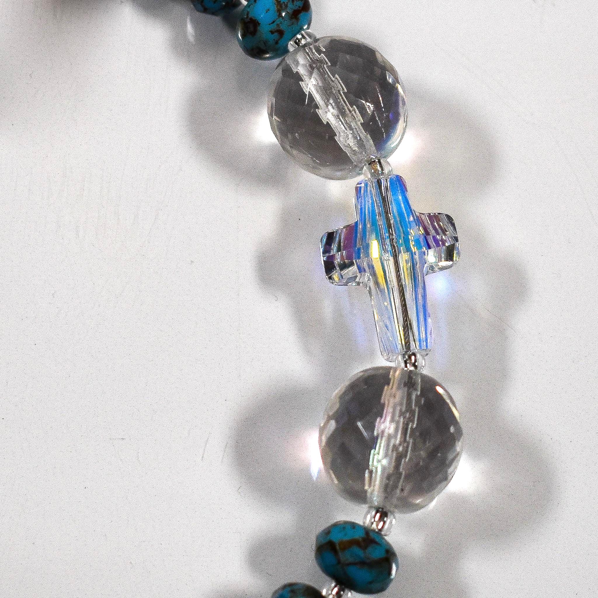 Close up view of crystal cross bead flanked by two round, faceted glass crystal beads, on white surface.