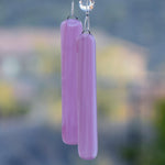 Two pieces of rectangular pink fused glass, hanging from bead-covered wire in front of blurred background of a house and a mountain.