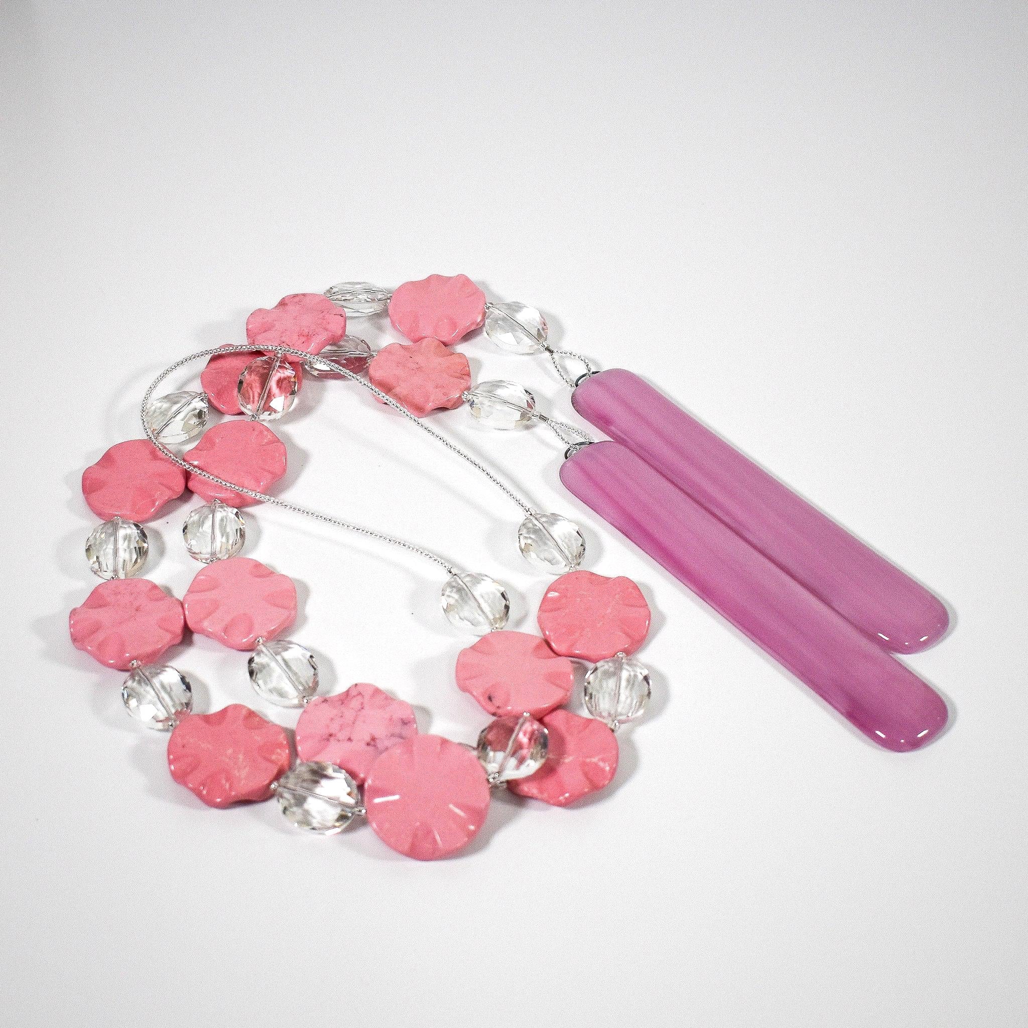 Pink magnesite stone wind chime made by Cinjo Handmade coiled on a white surface with 14 flat, wavy, round magnesite beads strung with oval glass crystal beads, strung on a single stainless steel wire with a piece of pink fused glass at each end.