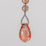 A teardrop-shaped pink and white crystal bead hanging from a wire chain that is covered with seed beads. The bead is faceted and has a translucent appearance.