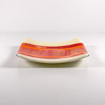 Square fused glass tray with vanilla cream colored base and a striped and streaky design of red, orange and white glass. Tray is 6&quot; square with upturned corners. Sitting on a white surface.