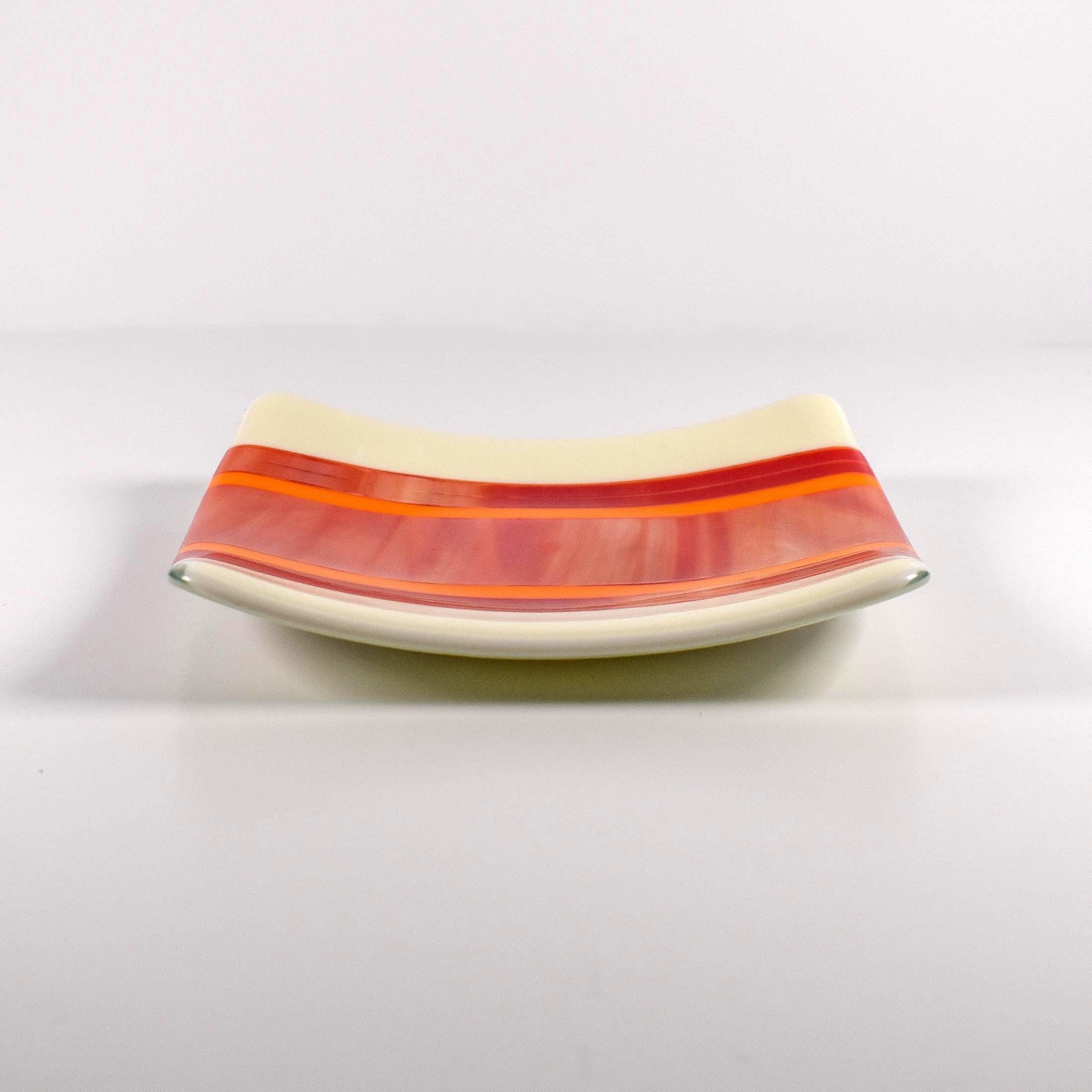 Square fused glass tray with vanilla cream colored base and a striped and streaky design of red, orange and white glass. Tray is 6&quot; square with upturned corners. Sitting on a white surface.