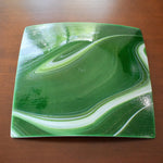 Backside of a square green glass plate showing white swirl design on sparkly aventurine green glass. The plate has a glossy finish and a subtle sparkle.