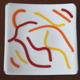 Close up view of orange, red and yellow abstract design on vanilla cream fused glass tray.