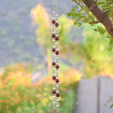 Large cranberry red jade stones beaded with glass and crystals, anchored by two pieces of dark cranberry pink fused glass, hanging vertically from a tree.