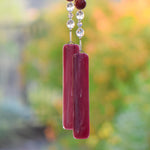 Two pieces of dark cranberry pink fused glass hanging vertically, attached to beaded wire.