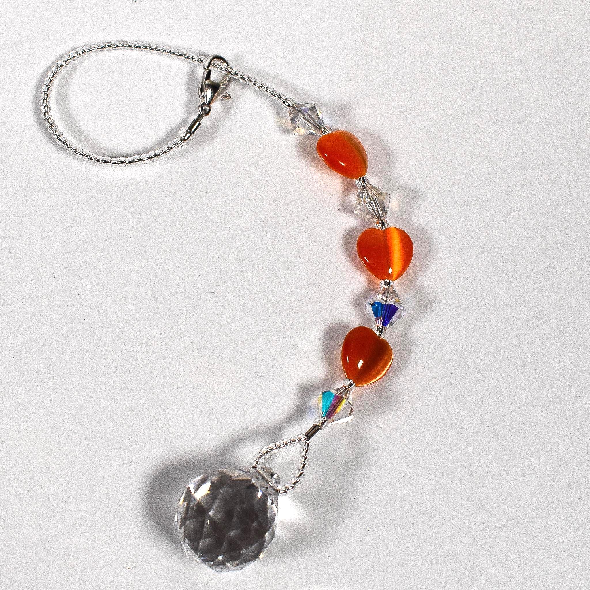 Small glass sun catcher made with small orange hearts, crystal bicones and a crystal prism, coiled up on white background.