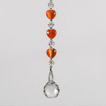 A crystal sun catcher with three orange heart-shaped beads. The suncatcher ends with a clear crystal ball.