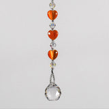 A crystal sun catcher with three orange heart-shaped beads. The suncatcher ends with a clear crystal ball.