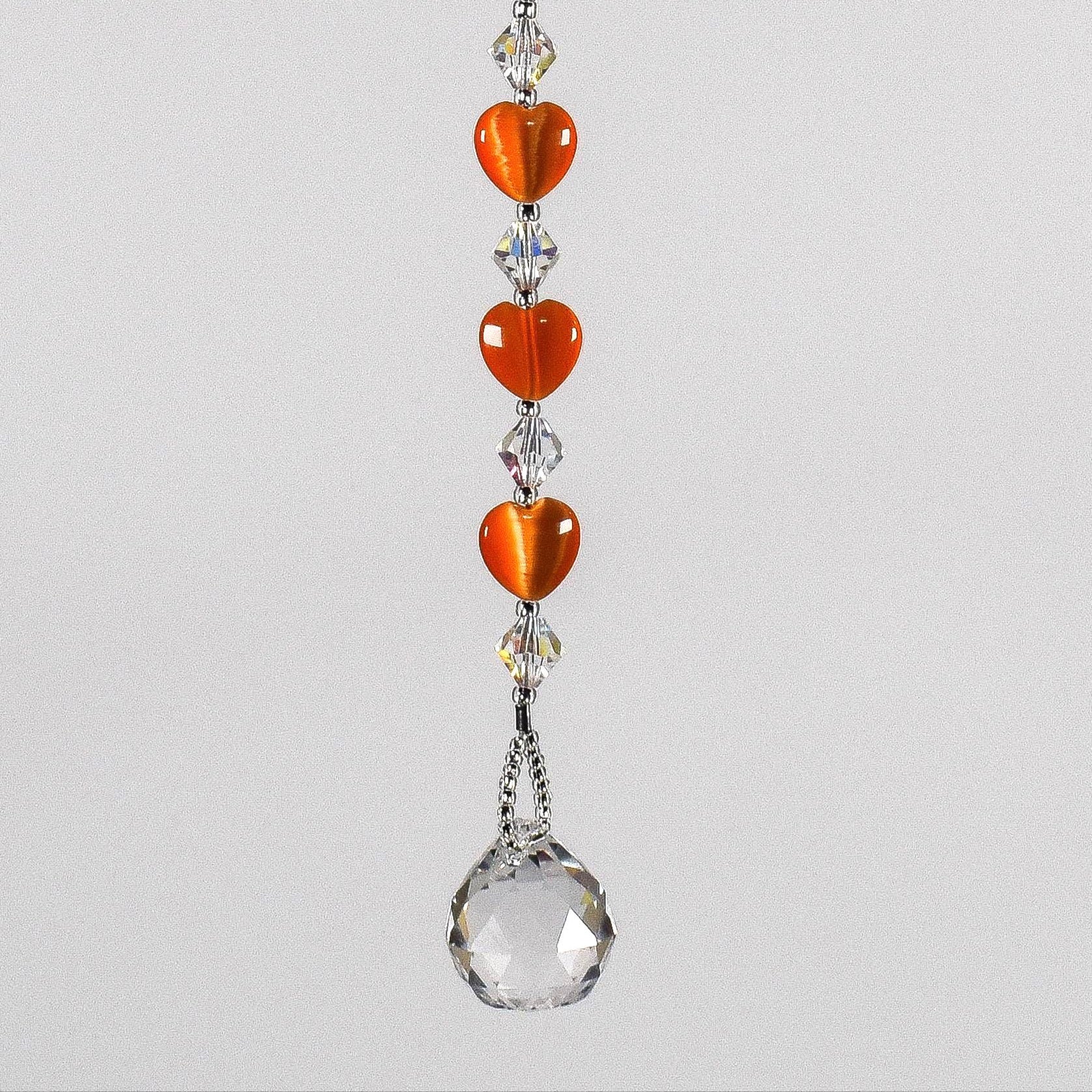 A crystal sun catcher with three orange heart-shaped beads. The suncatcher ends with a clear crystal ball.