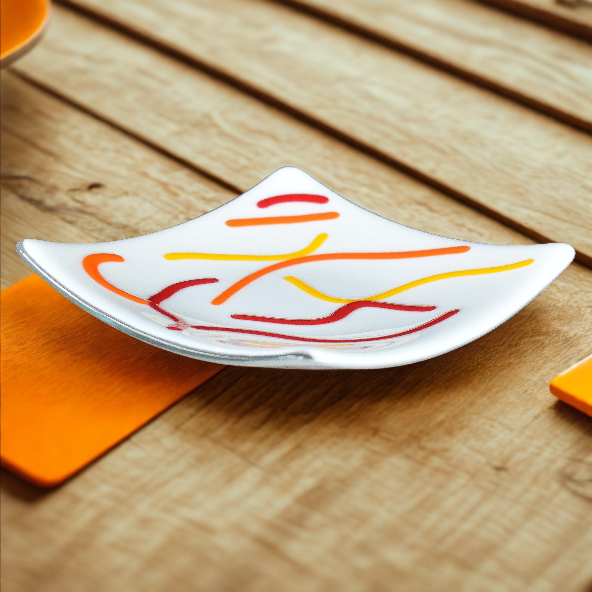 Creamy white square glass plate, viewed from an angle, on a wood slatted table with orange decor.