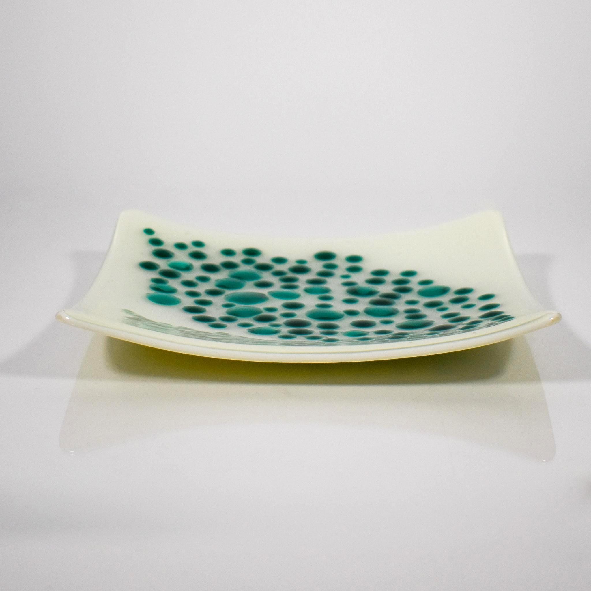 Square tray made of kiln formed glass in vanilla cream with teal green, circular pieces on top in a random, diamond-shaped pattern, against white background. Viewed from the side.