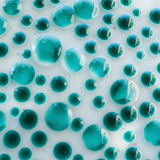 A close-up of a surface covered in teal-colored, translucent, spherical shapes of varying sizes. The spheres are densely packed, creating a bubbly, textured appearance. The background is a light, off-white color, providing contrast to the teal spheres. The image has a glossy, reflective quality.