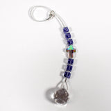 Small sun catcher with six purple crystal cube beads, a single crystal cross in paradise shine color, anchored by glass crystal prism. Flat on white surface.