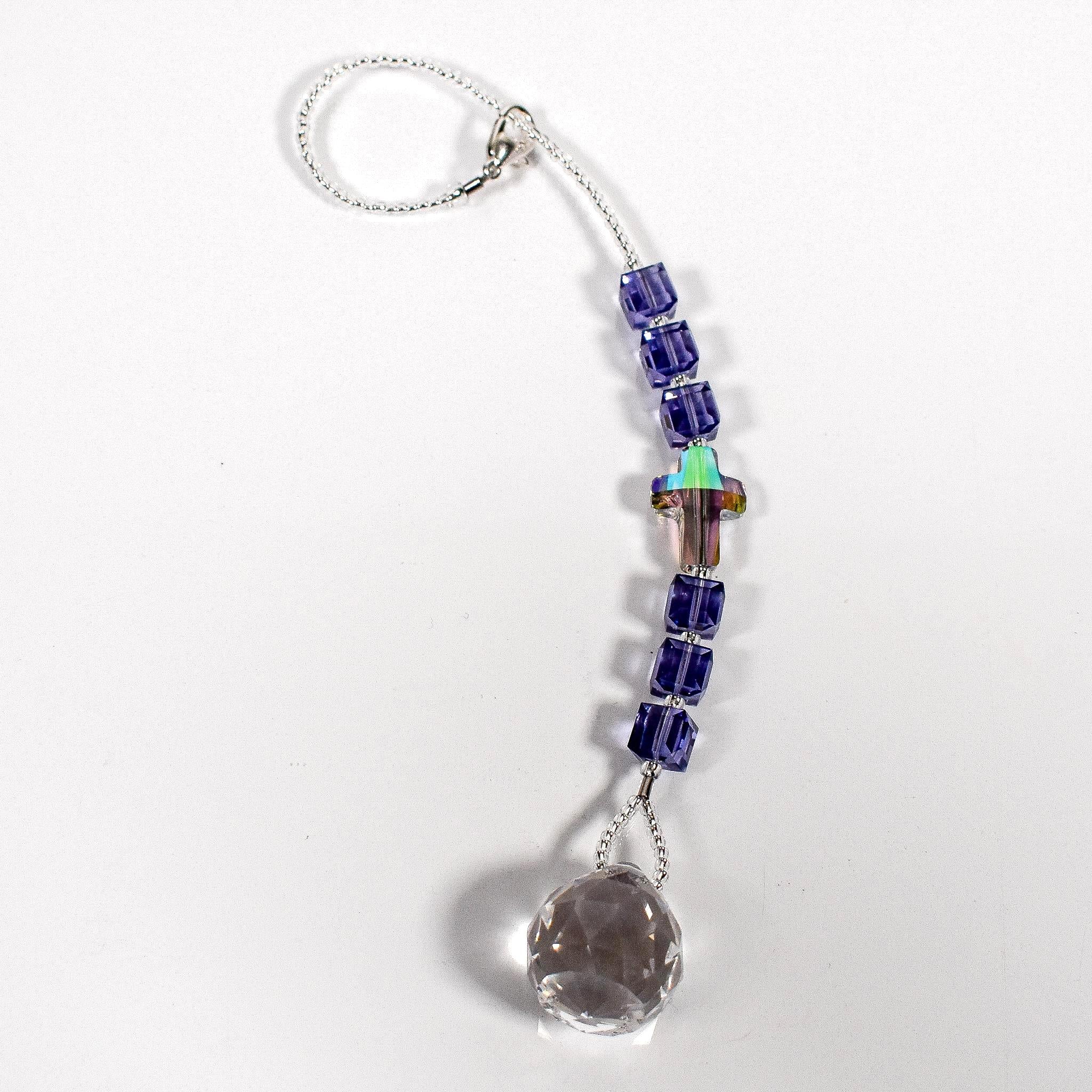 Small sun catcher with six purple crystal cube beads, a single crystal cross in paradise shine color, anchored by glass crystal prism. Flat on white surface.