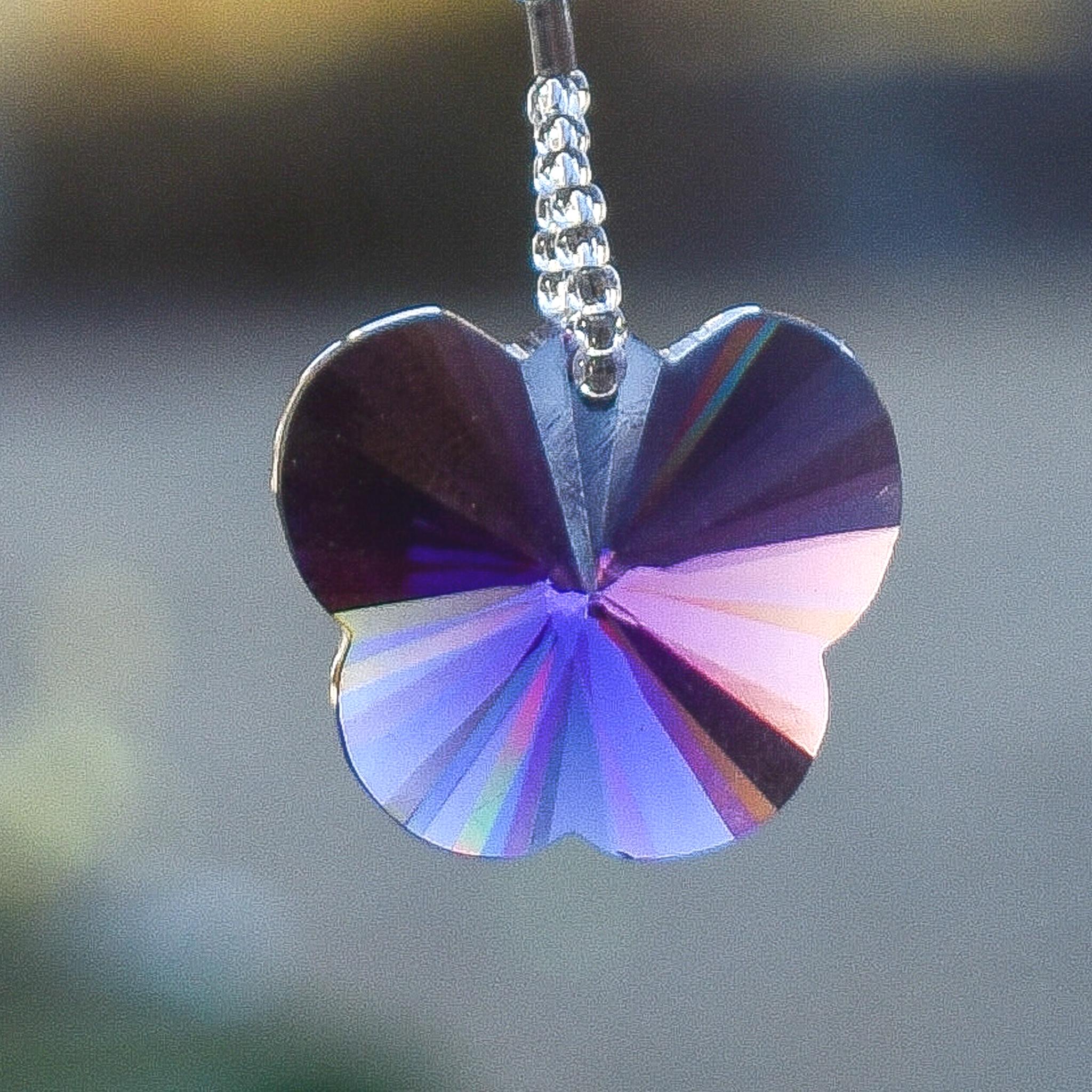 A purple crystal butterfly charm hanging from a wire lined with silver-lined seed beads.