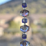A strand of iridescent purple and clear iridescent glass beads in a hexagonal shape. The beads are strung on a s wire and hanging vertically.