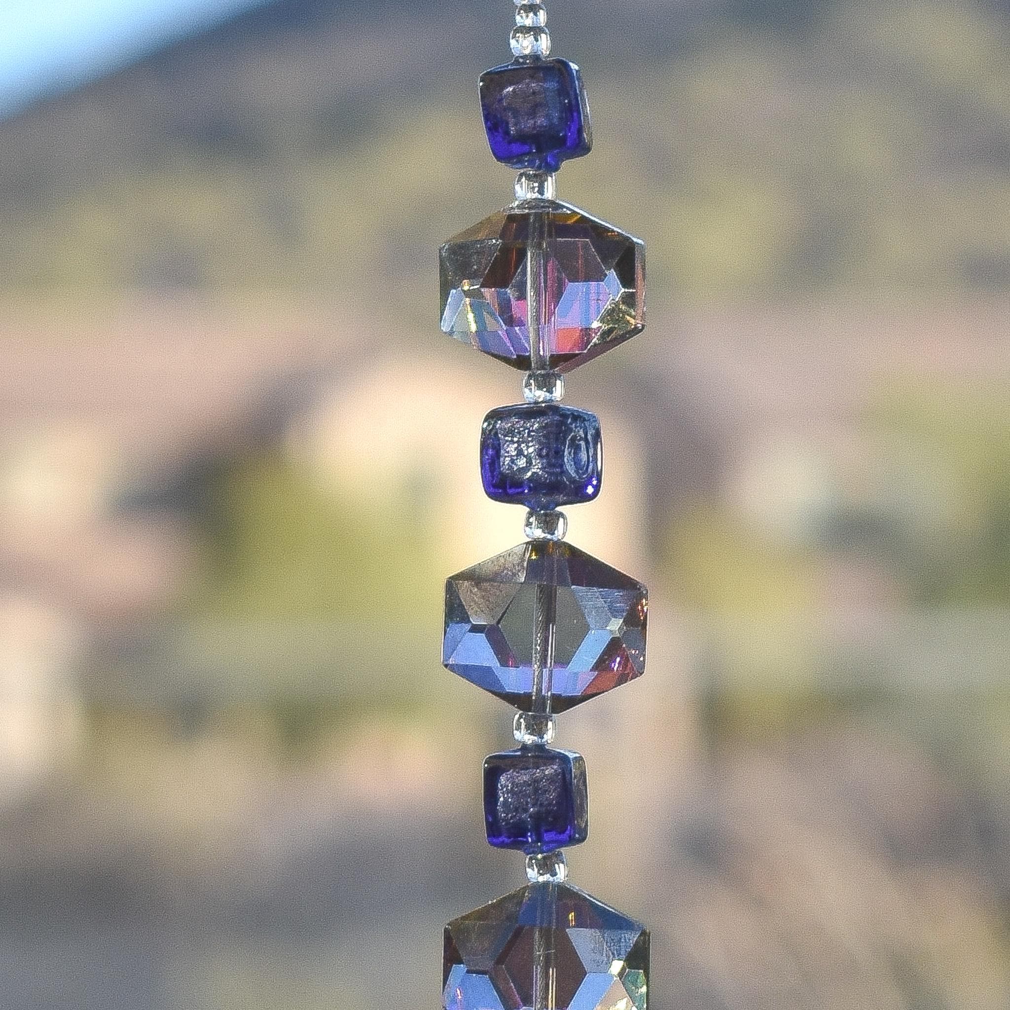 A strand of iridescent purple and clear iridescent glass beads in a hexagonal shape. The beads are strung on a s wire and hanging vertically.