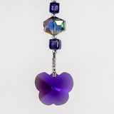A purple butterfly-shaped crystal charm hanging from a wire covered in silver-lined seed beads with a purple crystal bead and a iridescent crystal bead. White background.