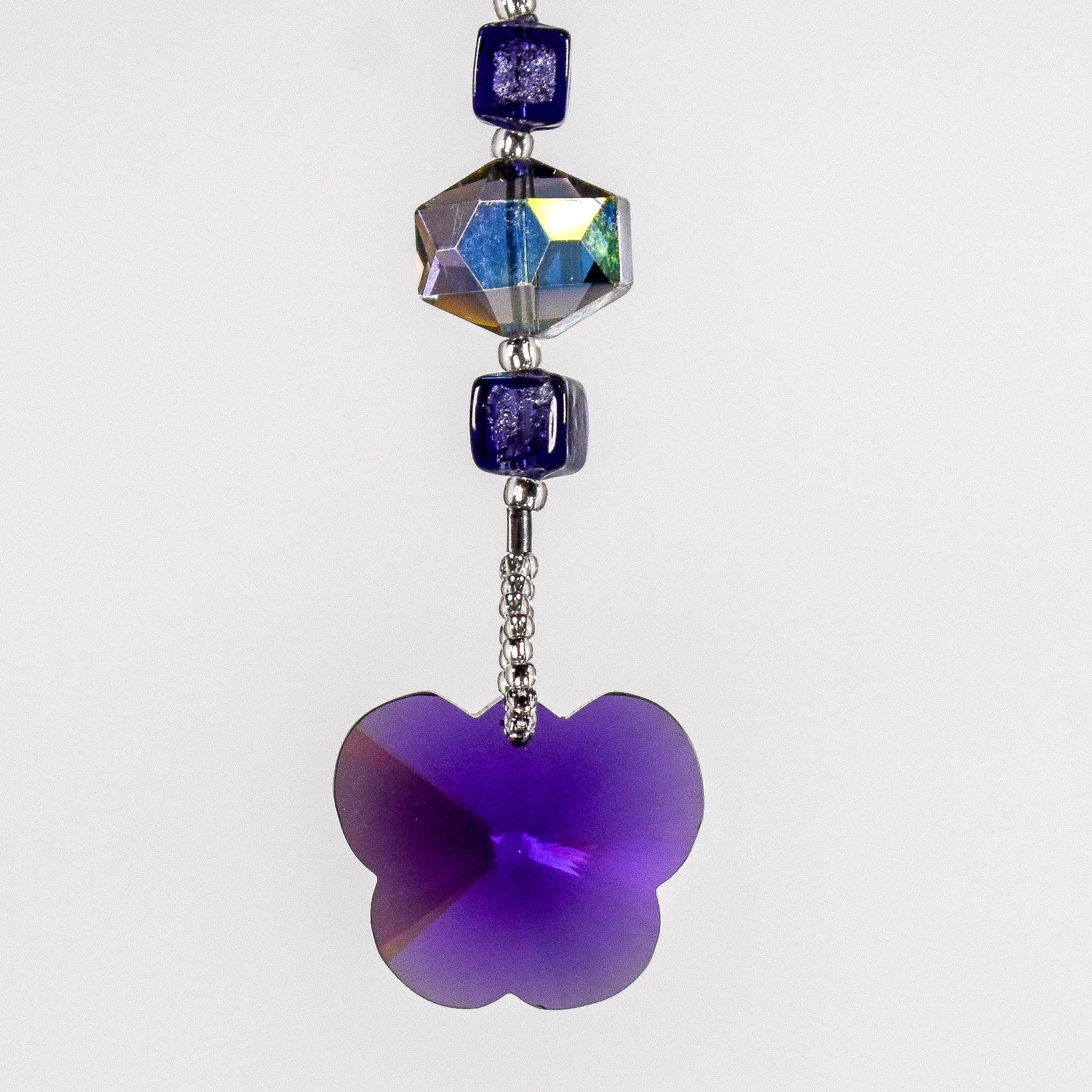 A purple butterfly-shaped crystal charm hanging from a wire covered in silver-lined seed beads with a purple crystal bead and a iridescent crystal bead. White background.