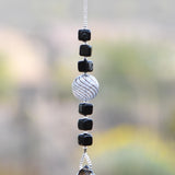 Small sun catcher hanging vertically in front of blurred background, made with six Murano glass cube beads flanking a large, round swirly bead and anchored by a large smoky quartz pendant.