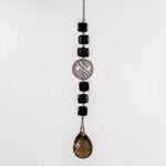 Small sun catcher hanging vertically in front of white background, made with six Murano glass cube beads flanking a large, round swirly bead and anchored by a large smoky quartz pendant.
