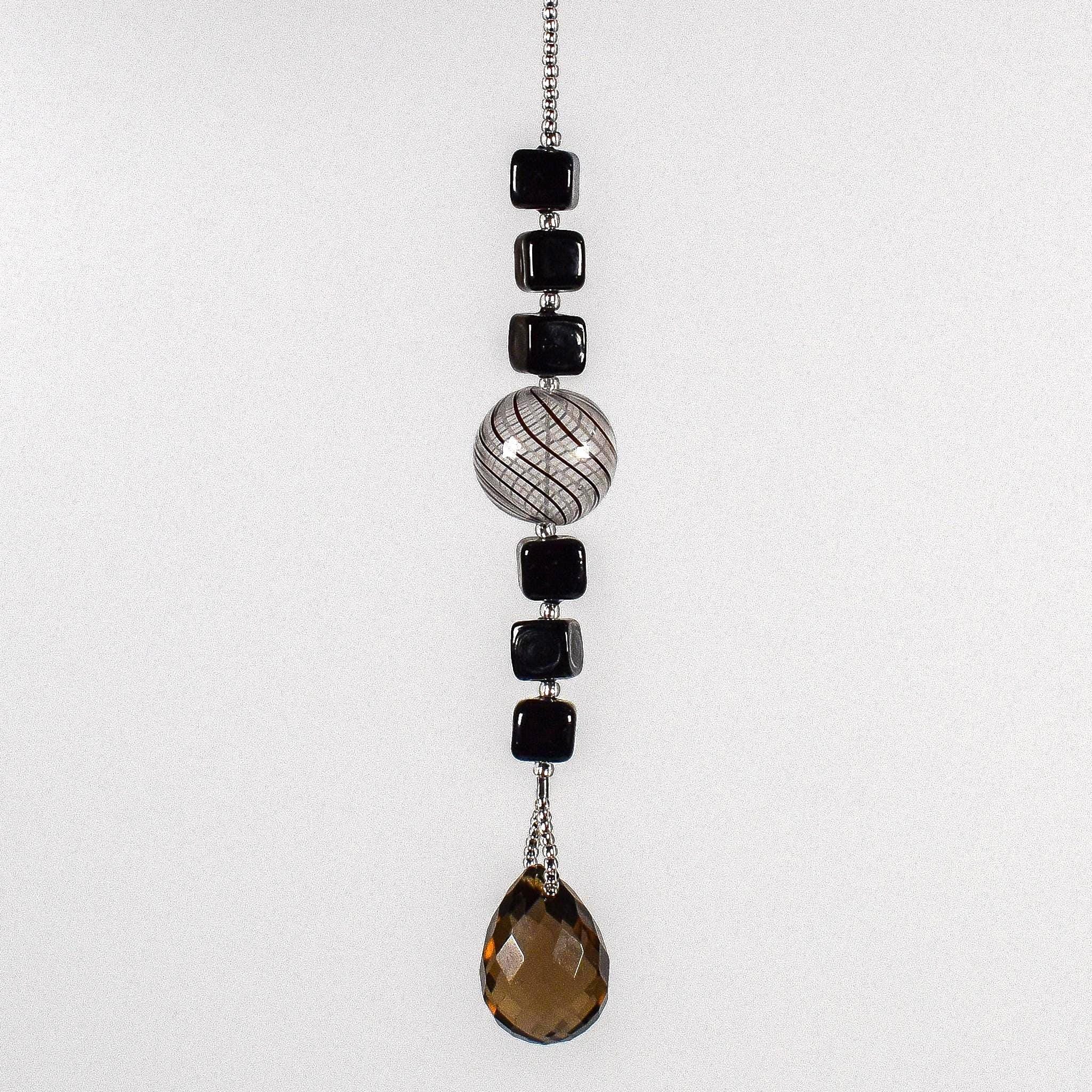 Small sun catcher hanging vertically in front of white background, made with six Murano glass cube beads flanking a large, round swirly bead and anchored by a large smoky quartz pendant.