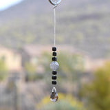 Small sun catcher hanging vertically in front of blurred background, made with six Murano glass cube beads flanking a large, round swirly bead and anchored by a large smoky quartz pendant.